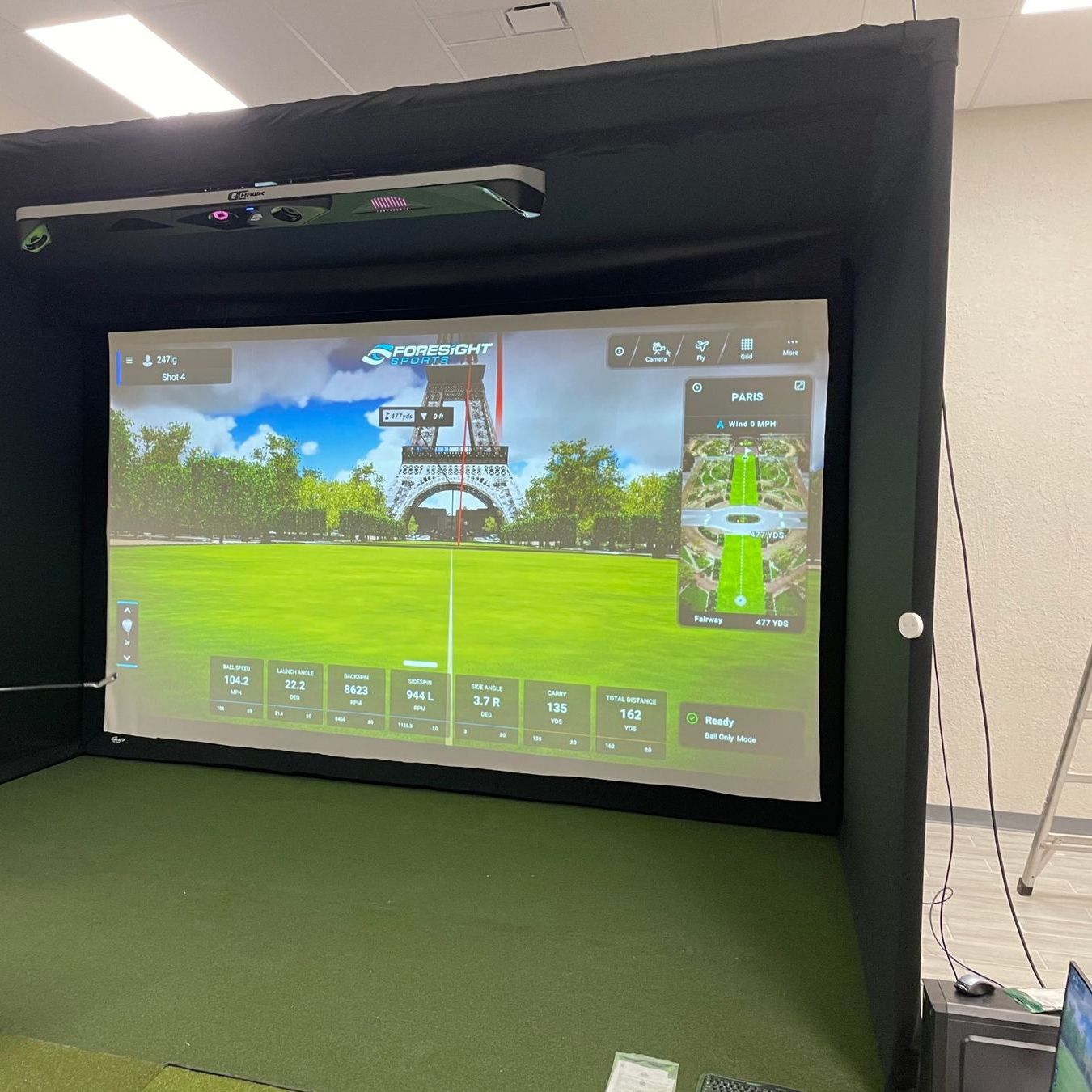 Simulator enclosure with ceiling-mounted launch monitor in a large white room.