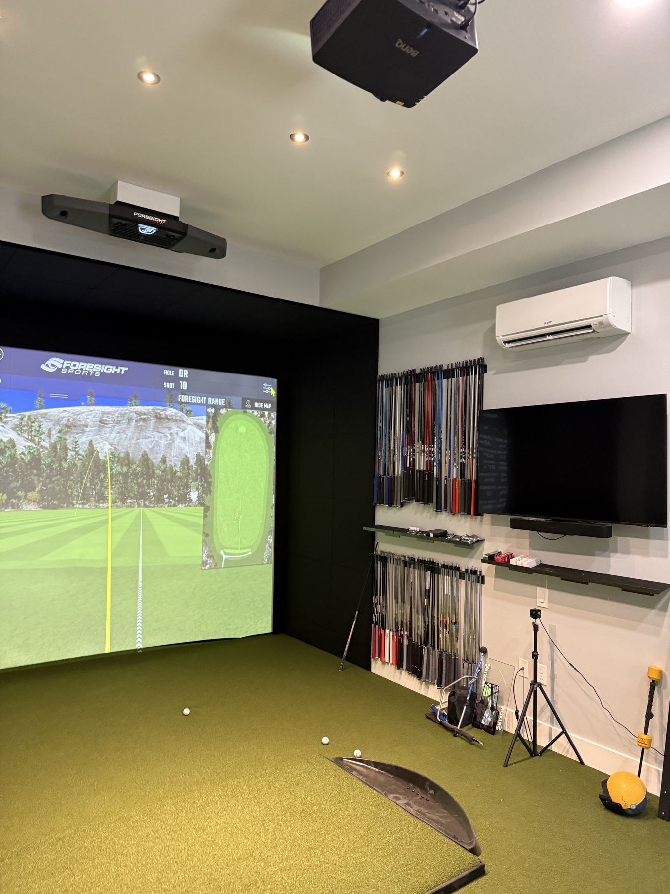 Wide view of a private studio simulator with projector, overhead launch monitor, mini-split and shaft wall.