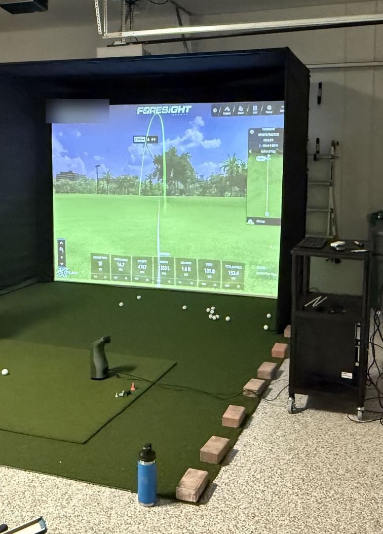 Freestanding simulator enclosure in a garage with a floor-side launch monitor on the hitting mat.