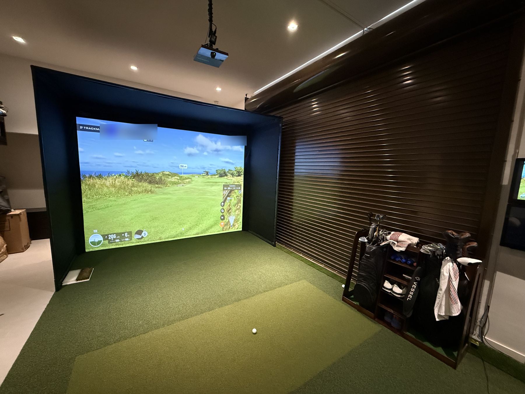 A modular simulator enclosure installed in a garage, with turf and a ceiling projector.